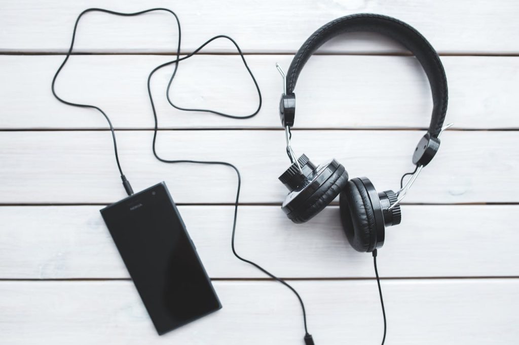 Black vintage headphones connected to a smartphone on a wooden background. Ideal for music themes.